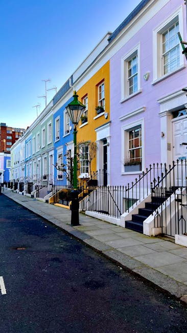 A row of colorful terraced houses along a city street, featuring pastel-colored facades in shades of blue, yellow, purple, and white. Each house has a small front staircase with black metal railings, 